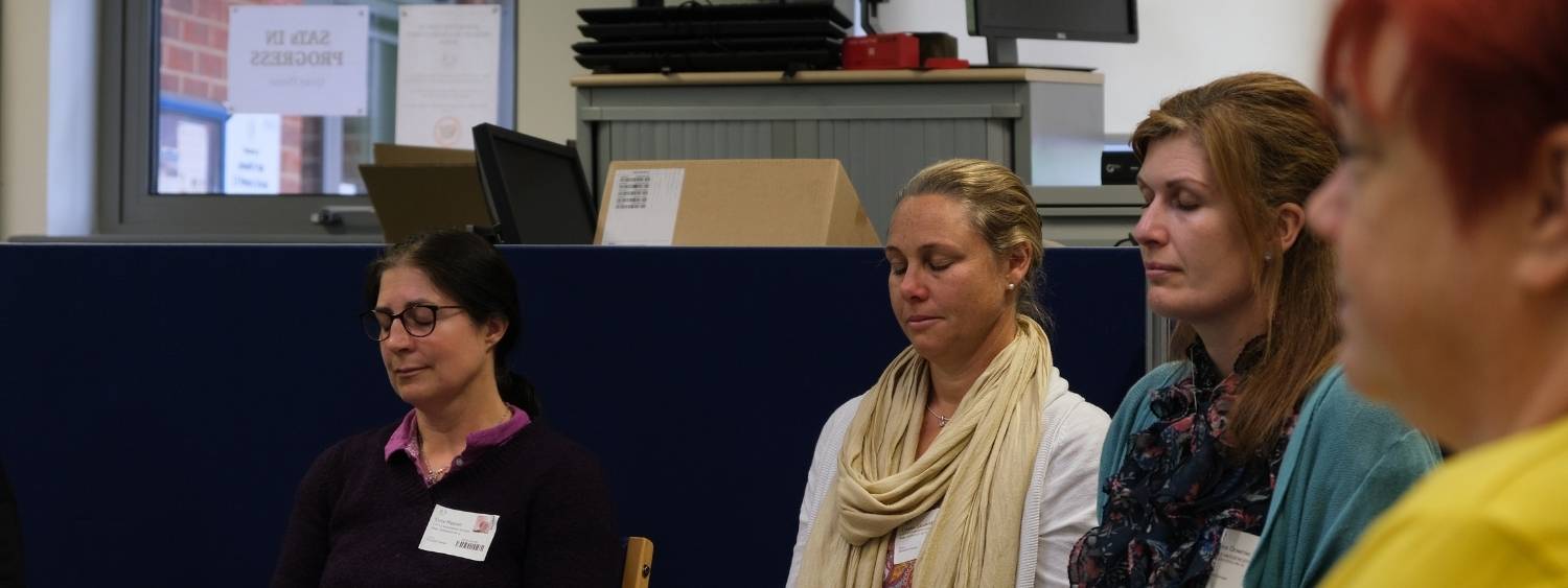 Female teaching staff sit with their eyes closed whilst taking part in the stilling practice.